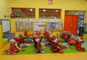 Dzieci siedzą w czterech rzędach, unoszą nad głową czerwone chusteczki.